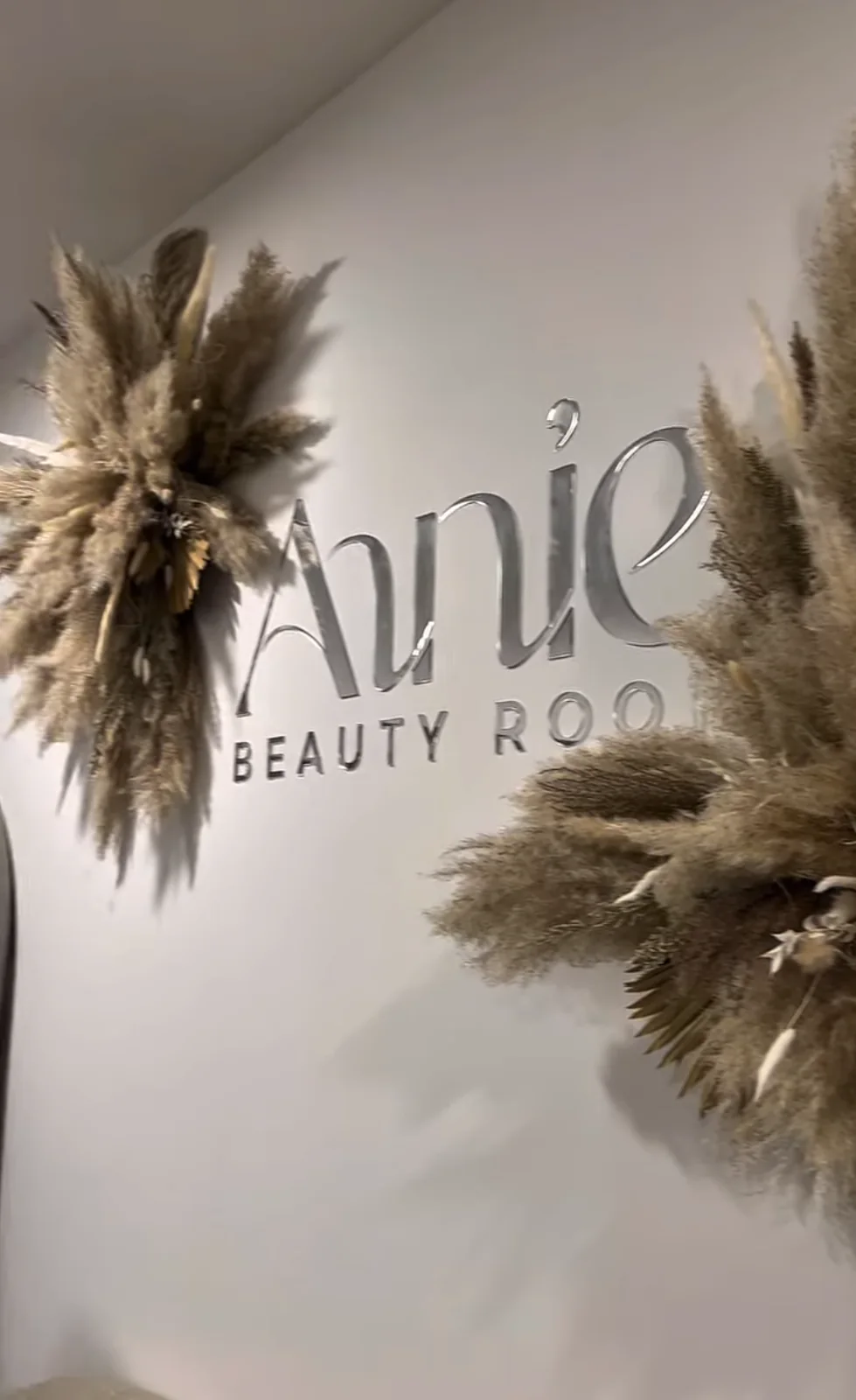 Srebrn napis Annie Beauty Room na steni studia s suhim cvetjem